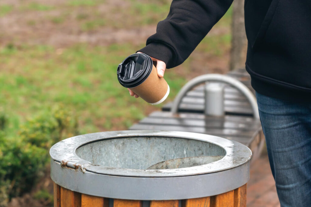 image of someone putting an empty coffee cup in the bin.