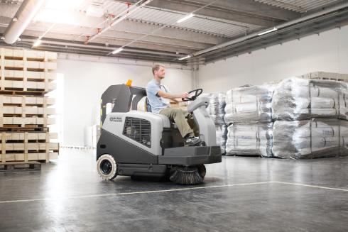 the Sw5500 ride on sweeper brushing the floor of a warehouse.